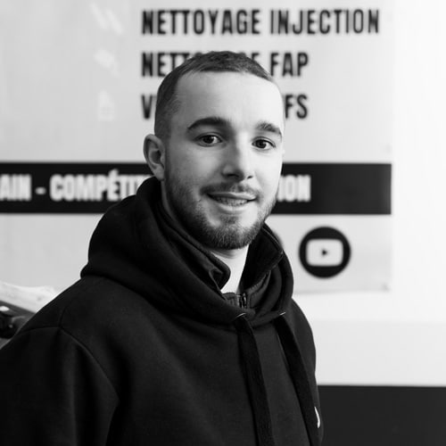 Services auto : Nettoyage Injection et FAP en vidéo Jeune homme souriant en sweat à capuche noir devant un panneau mentionnant 'NETTOYAGE INJECTION', 'NETTOYAGE FAP' et un logo YouTube.