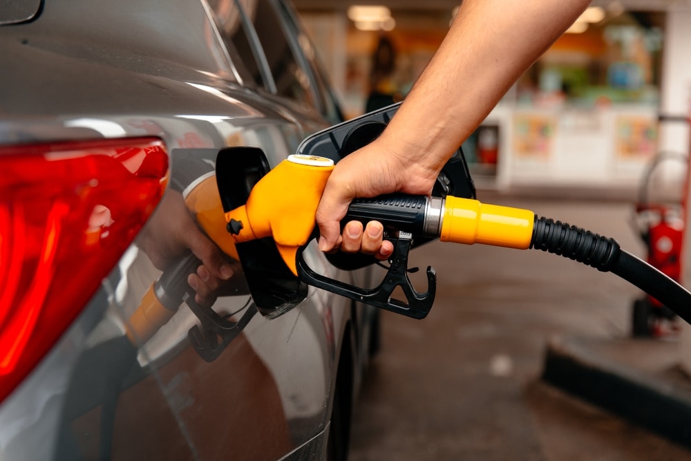 Main insérant un pistolet à essence jaune dans le réservoir d'une voiture grise à la station-service.